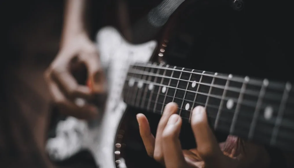 Hände an Griffbrett und Saiten einer E-Gitarre